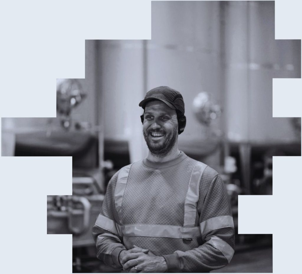 An image of a smiling shift worker in a manufacturing environment to illustrate how the future of shift work will be key to adapting to growing workforce expectations as well as increasing risk and regulation, volatile operating landscapes and changing production environments